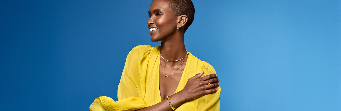 A woman wearing yellow gold jewellery from Birks on a blue background.